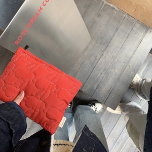 Outdoor shot of a red quilted rabbit pattern makeup pouch held by hand in a street setting
