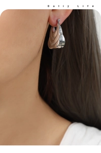 Close-up of silver geometric layered bag-style earrings on model with high polish finish