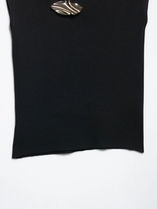 Detailed close-up of smooth black knit fabric with a polished leaf-shaped metal ornament