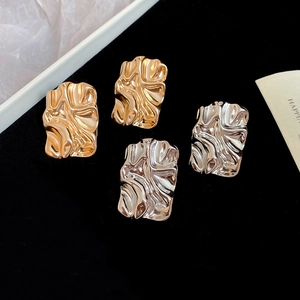 Detailed macro view of irregular crumpled gold and silver square metal stud earrings