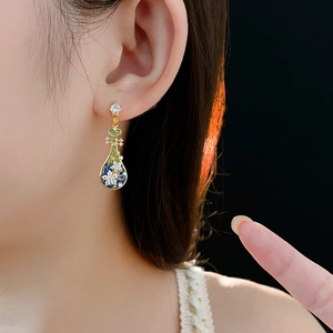 Dettaglio di orecchini a fiore vintage con smalto verde e perle su una modella