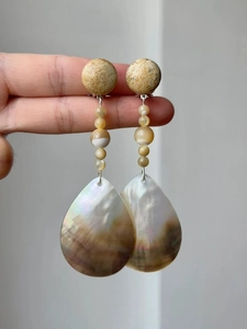 Macro shot of long drop earrings with natural stones and brown shells held by hand