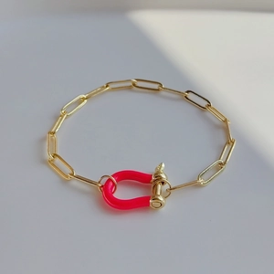 Detail of gold paperclip chain bracelet featuring a bright pink enamel horseshoe clasp