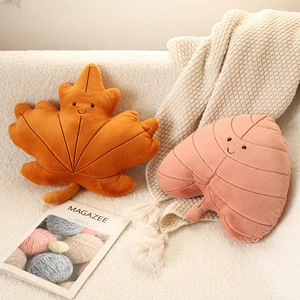 Plush leaf pillows with cute smiles in orange maple and pink leaf shapes on a white sofa