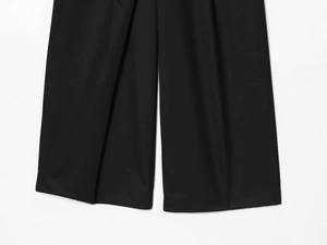 Detail shot of black wide-leg trousers showing premium woven fabric texture and hem stitching