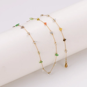 Gold chain necklace with irregular colorful stones on a white cylinder stand