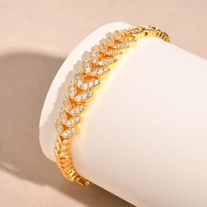 Detail of leaf-shaped gold bracelet with white zircon inlay on white jewelry display