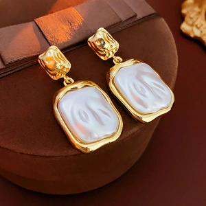 Macro detail of gold vintage wrinkled square earrings with white baroque pearl inserts