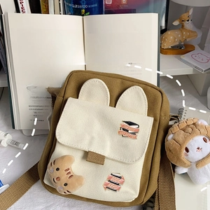 Brown canvas crossbody bag with bunny ears and book nerd badges on a desk