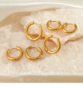 Three pairs of golden satin matte round hoop earrings in different sizes on white mineral stones