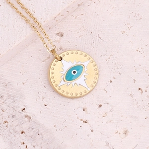 Close-up of golden evil eye charm necklace with blue enamel on natural stone background