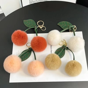 Detail of plush cherry keychains in four colors with faux fur balls and green leather leaves