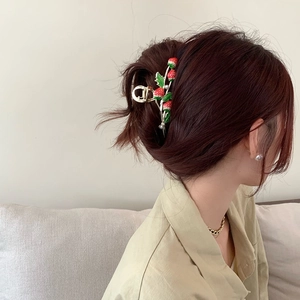 Detail of golden strawberry hair claw clip with CD logo on red-brown hair styling