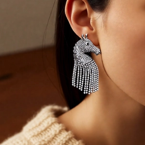 Close-up of horse head earrings with shimmering rhinestone tassels on a model