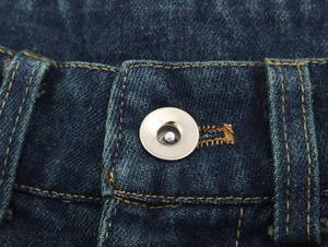 Primer plano macro de jeans de mezclilla azul oscuro con botón metálico y costuras amarillas
