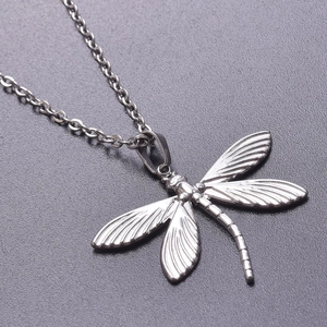 Macro shot of silver dragonfly pendant showing detailed wing textures and thin chain links