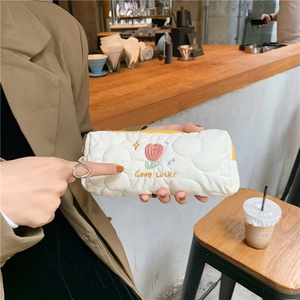 Detail of white quilted pouch featuring pink tulip embroidery and Good Luck text