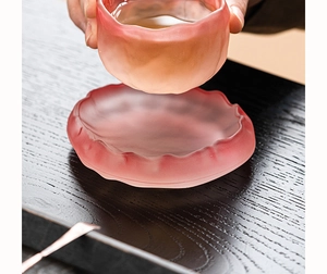Detailed view of pink glacier tea cup with lotus leaf edge on dark wood table