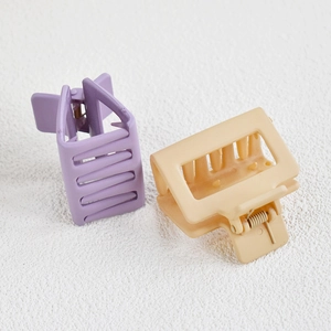 Close-up of matte square hair claw clips in purple and beige on a textured surface