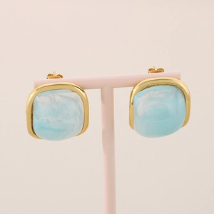 Détail de boucles d'oreilles en résine marbre bleu clair avec monture dorée en acier