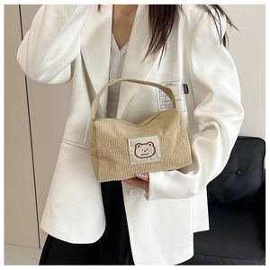 Detail view of beige corduroy handbag featuring a cute cartoon bear patch on a white suit