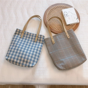 Detail of vintage plaid canvas tote bags with leather handles on a white quilted bed