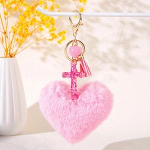 Detail of pink plush heart and resin cross keychain with tassel and gold metal hardware