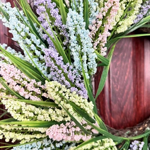 Close-up of a colorful faux lavender berry wreath hanging on a dark red wooden door