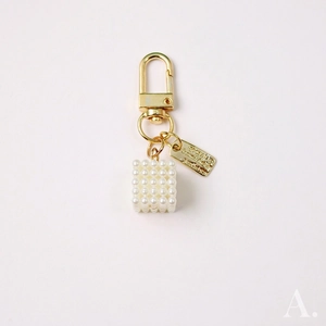 Detail of handmade woven pearl cube keychain with gold lobster clasp and metal tag