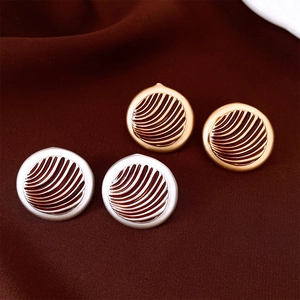 Detailed macro view of vintage round button earrings with wave textures on dark velvet