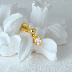 Close-up of gold cartilage stud earring with round clear gemstone on a ceramic flower