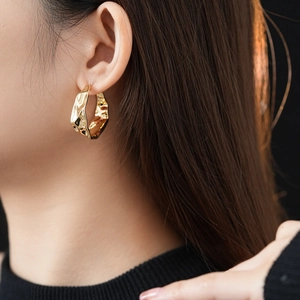 Detailed close-up of golden wrinkled C-shape earrings with a liquid metal texture