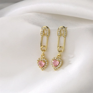 Vue macro de boucles d'oreilles trombone dorées avec pierre rose en cœur sur soie