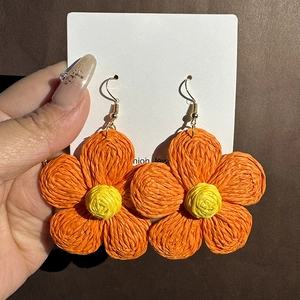 Close-up of handmade woven raffia flower earrings with orange petals and yellow centers