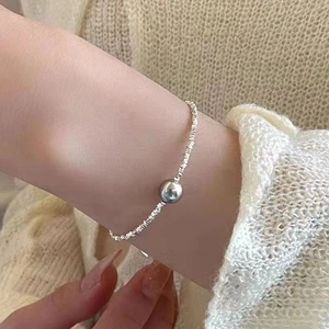 Close-up of a silver pearl bracelet with zircon heart on a model wearing knitwear