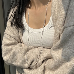 Detailed view of a long pearl necklace layered over a beige sweater for an elegant look
