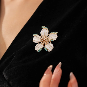 Détail d'une broche fleur en émail blanc avec perles turquoise sur velours noir