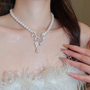 Close-up of elegant pearl necklace with crystal bow pendant worn by a model in soft lighting