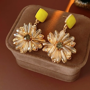 Detail von Blumenohrringen mit Goldmetall, gelben Steckern und grünem Edelstein
