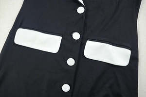 Detail of black dress featuring contrasting white buttons and symmetrical pocket flaps