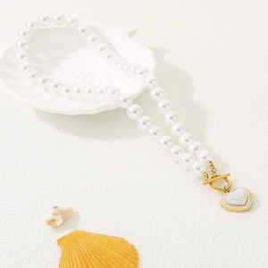 Macro view of a pearl necklace with a heart pendant and shell tray on white background