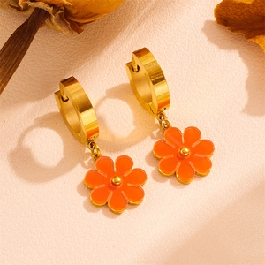 Detailed close-up of golden hoop earrings with orange daisy flower charms on leather