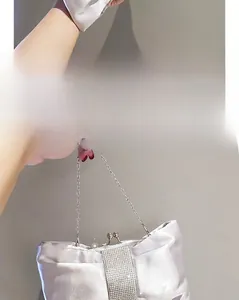 Detail einer silbernen Satin-Abendtasche mit Strass-Schleife und Metallkettenriemen