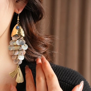 Detail of vintage fish-shaped earrings with shell scales and blue evil eye accent