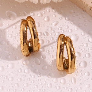 Detailed close-up of double-layered golden C-shaped earrings on a wet stone surface