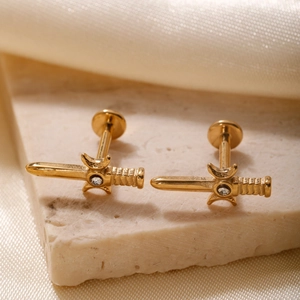 Elegant gold dagger earrings with zircon stone on a stone pedestal with silk background