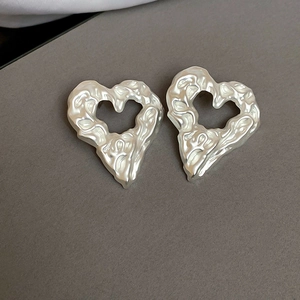 Detailed close-up of irregular heart earrings with molten lava texture in pearl white finish