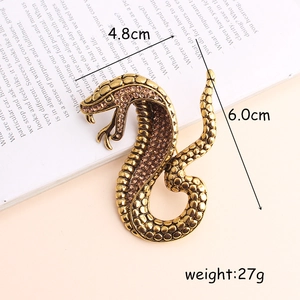 Golden snake safety pin brooch with crystals beside a book, dimensions 4.8cm by 6.0cm