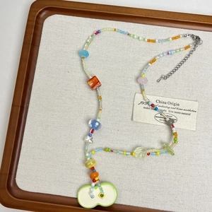 Detail shot of colorful glass beads necklace featuring a light green apple pendant charm