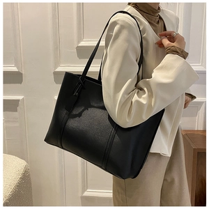 Side view of model carrying a large black soft leather tote bag against a white wall
